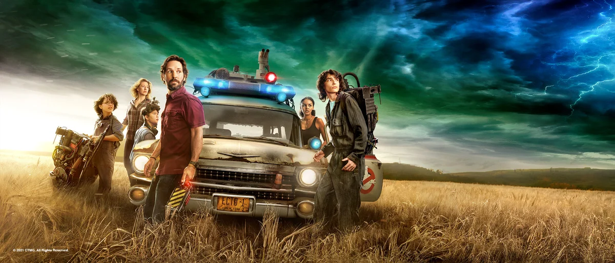 Ghostbusters: Afterlife cast beside the Ecto-1 car in official promotional artwork.